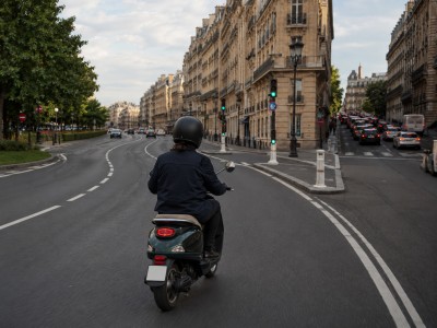 Scooter électrique 50cc roulant sur un boulevard européen fluide, alternative aux ruelles congestionnées pour économiser la batterie.