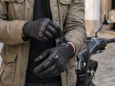 Motard ajustant la fermeture de gants moto d'été respirants avec protections des articulations à côté de son scooter