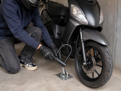 Jeune conducteur attachant un scooter 50cc avec un antivol en U à un point fixe dans un garage sécurisé.