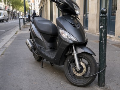Mauvaise pratique: scooter 50cc attaché avec un simple câble non fixé à un point fixe sur le trottoir.